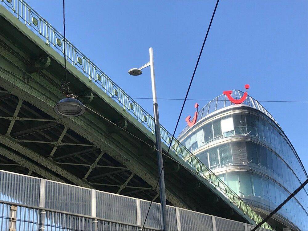 Ansicht eines modernen Bürogebäudes mit geschwungener Glasfassade neben einer grünen Brückenkonstruktion.