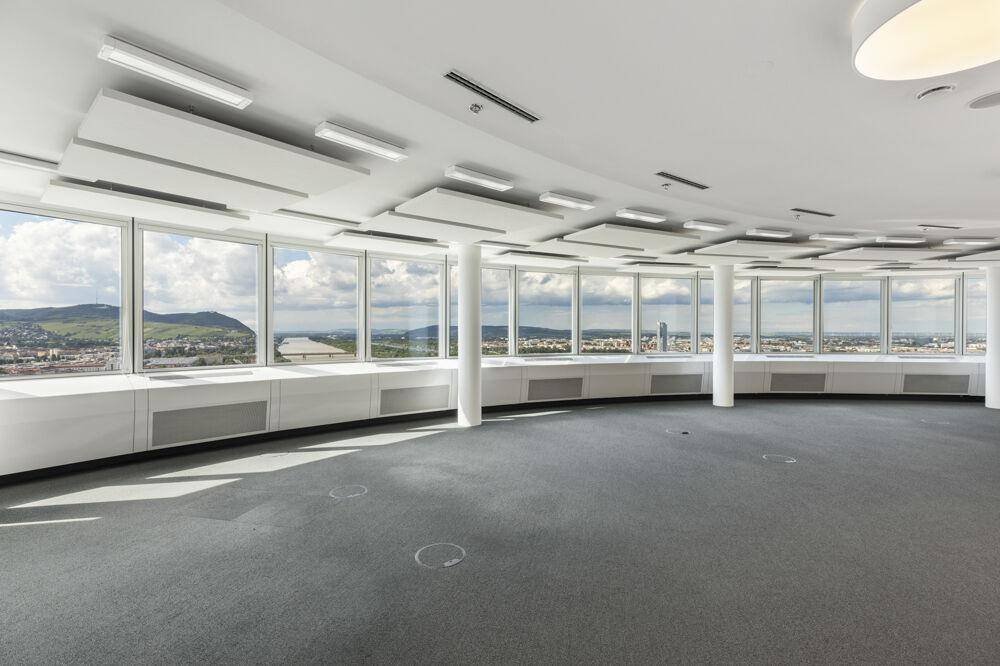 Leerer Büroraum mit Teppichboden und großen Panoramafenstern, die eine weite Aussicht bieten.