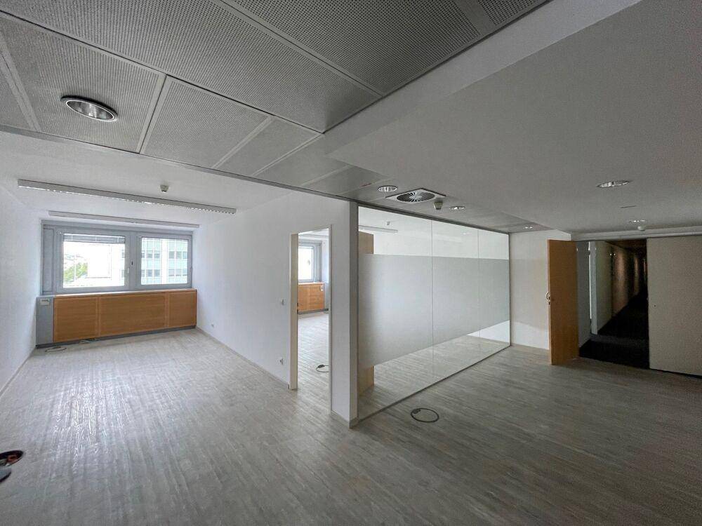 Helles Büro mit Glasabtrennung, abgehängter Decke und Holzverkleidung unter den Fenstern.