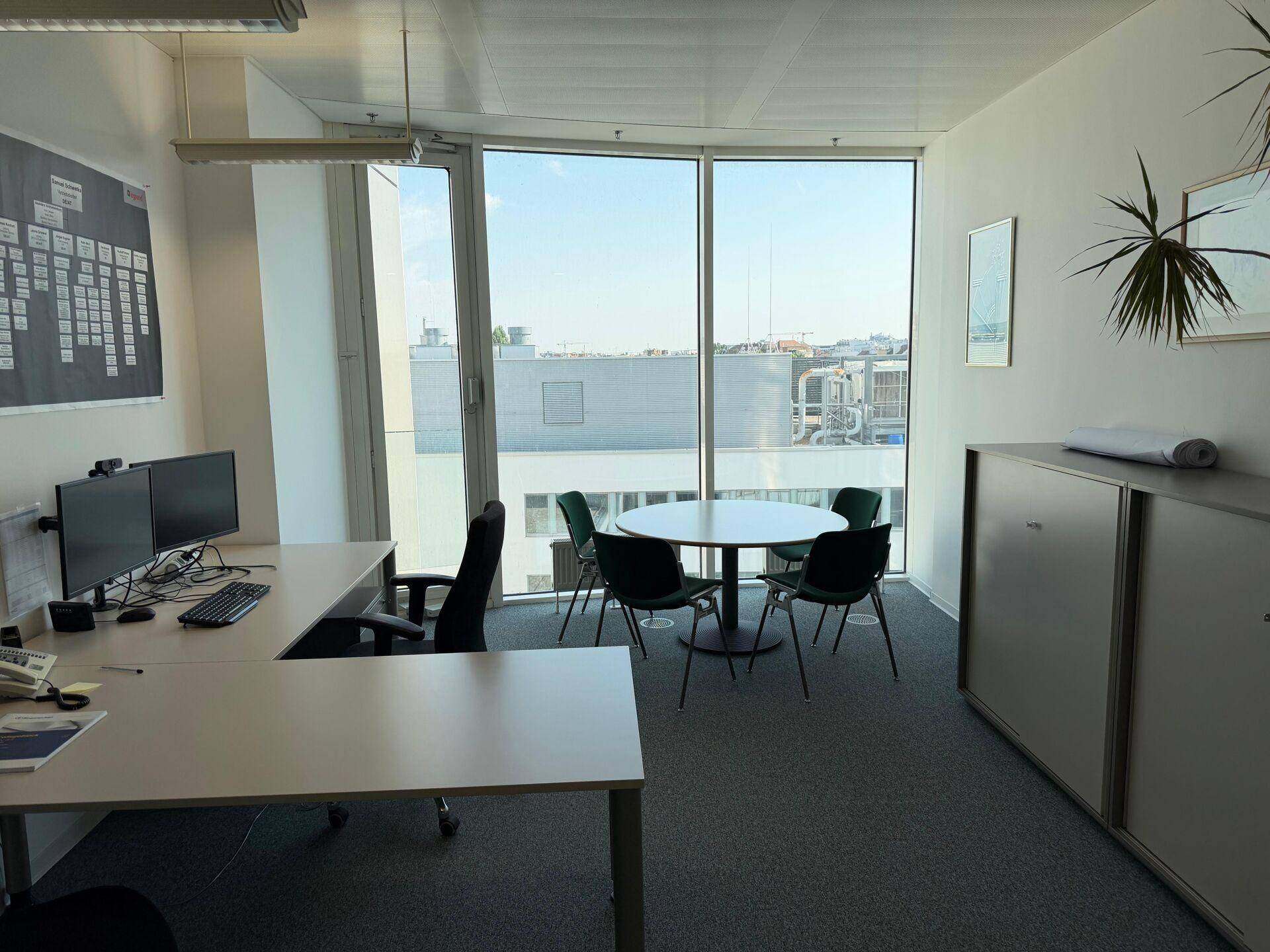 Büro mit zwei Arbeitsplätzen, Besprechungstisch und großen Fenstern mit Stadtblick.