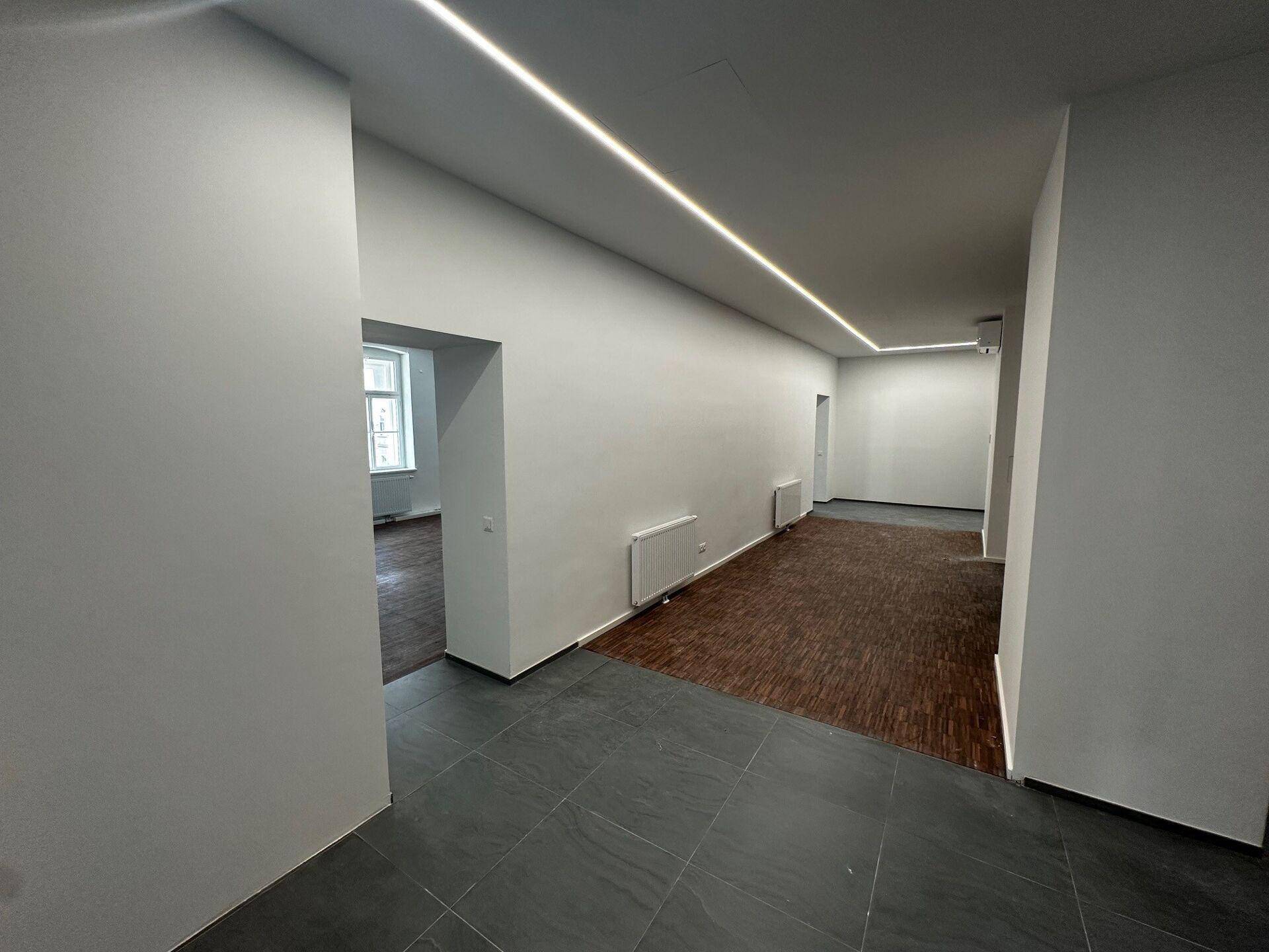 Übergangsbereich mit dunklem Fliesenboden, weißen Wänden und Blick in angrenzende Büroräume.