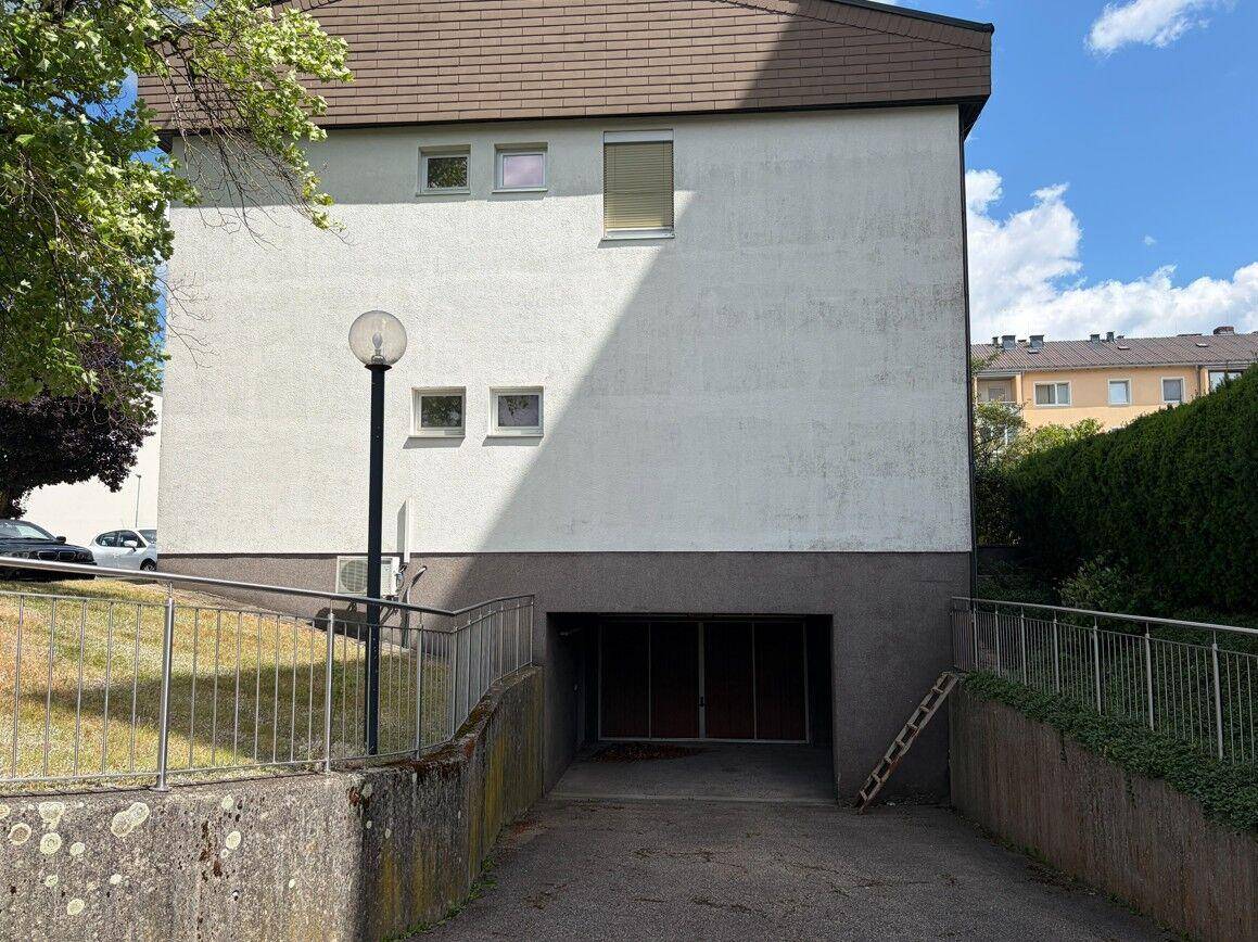 Rückseite eines Gebäudes mit Zufahrt zu einer Tiefgarage und weißer Fassade.