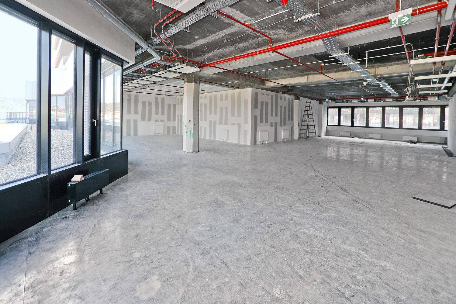 Geräumiger, unfertiger Bürobereich mit großen Fenstern und sichtbaren Deckeninstallationen, bereit für den Ausbau.