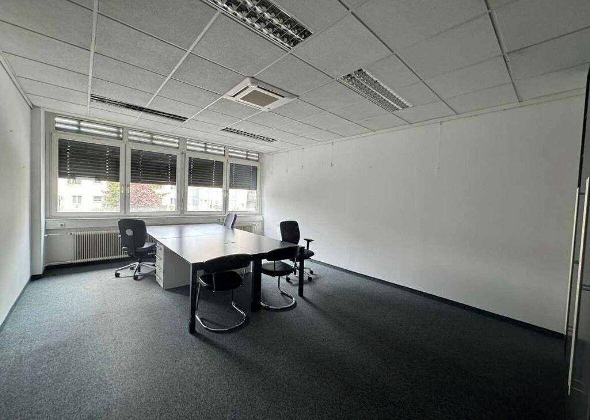 Geräumiges, unmöbliertes Büro mit Teppichboden, großen Fenstern und abgehängter Decke, bereit zur Einrichtung.