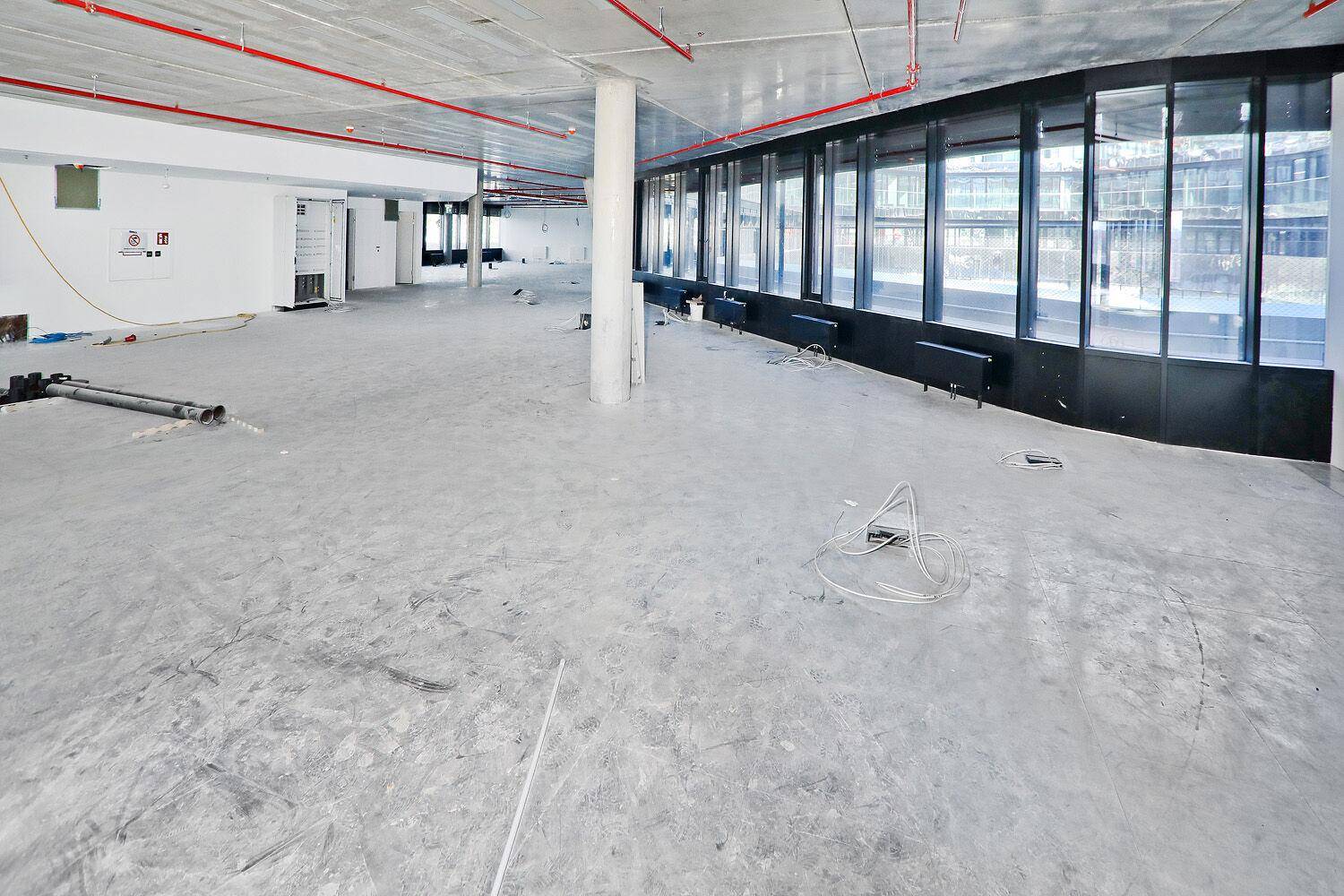 Geräumiger Büroraum im Rohbau mit Betonboden und großen Fenstern, die eine helle und offene Arbeitsumgebung schaffen und viel Potenzial bieten.