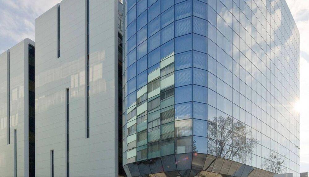 Nahaufnahme einer modernen Glasfassade mit reflektierenden Fenstern und klaren Linien unter blauem Himmel.