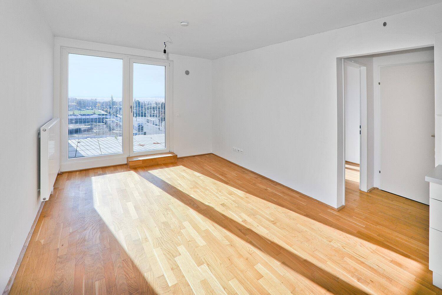 Lichtdurchfluteter Wohnraum mit großen Fenstern, Parkettboden und direktem Zugang zum Außenbereich.