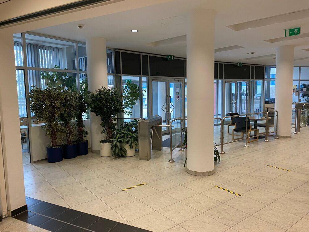 Heller Eingangsbereich mit Drehkreuzen, großen Fenstern, Fliesenboden und dekorativen Pflanzen.