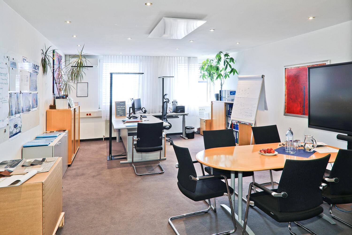 Helles Büro mit mehreren Arbeitsplätzen, einem runden Besprechungstisch und Pflanzen.