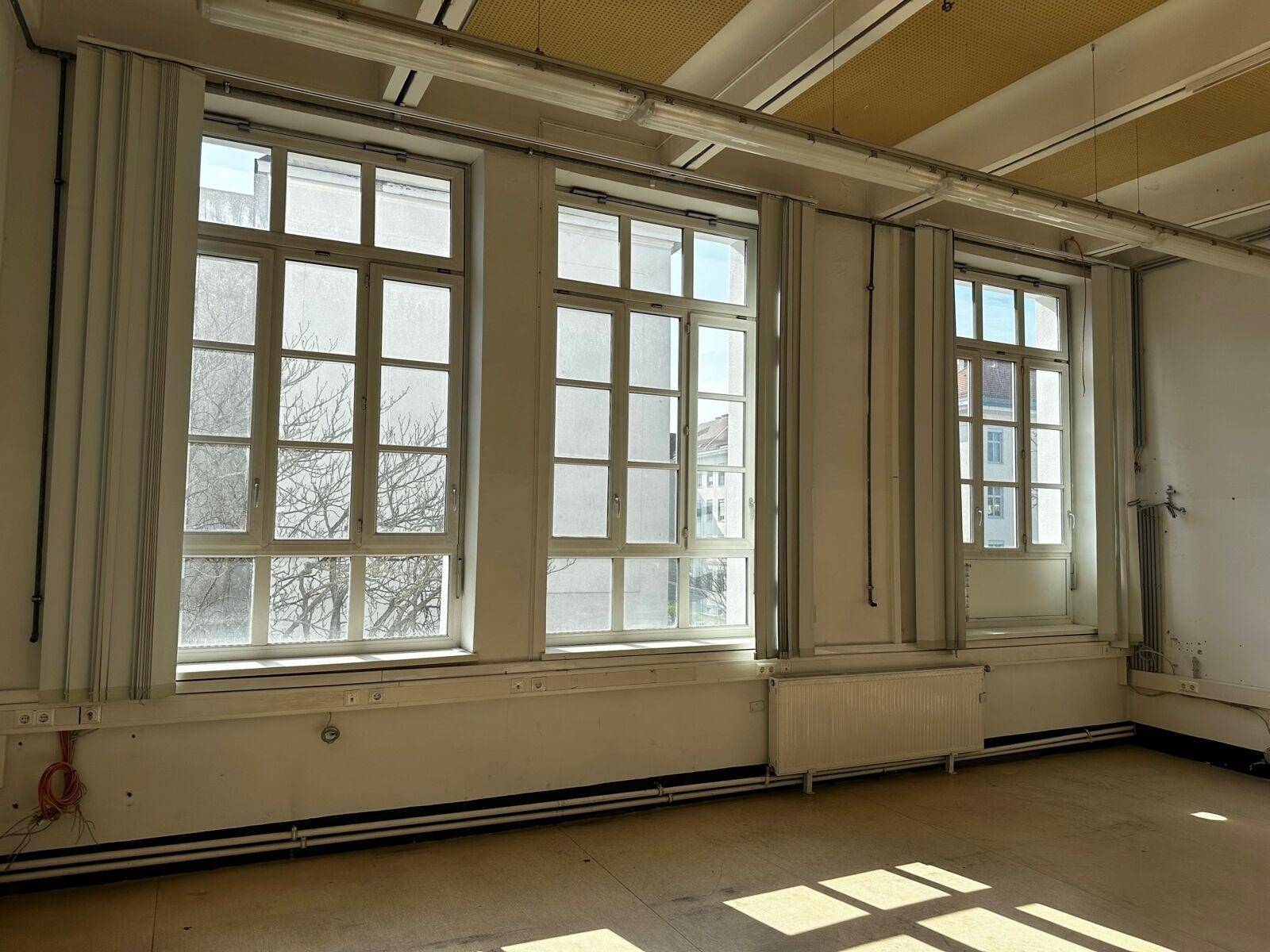 Heller Innenraum mit großen Sprossenfenstern, die viel Tageslicht hereinlassen, und Heizkörpern darunter.