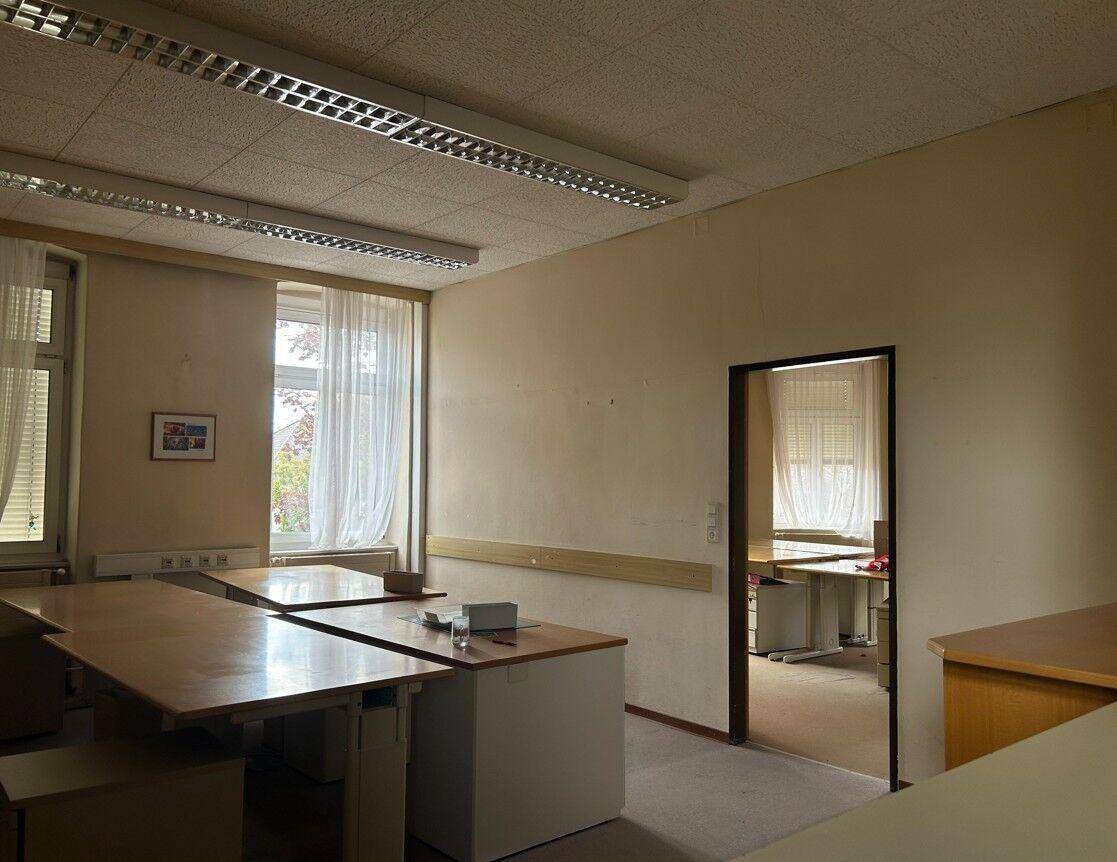 Bürofläche mit mehreren Arbeitsplätzen und einem Durchgang zu einem weiteren Büroraum.