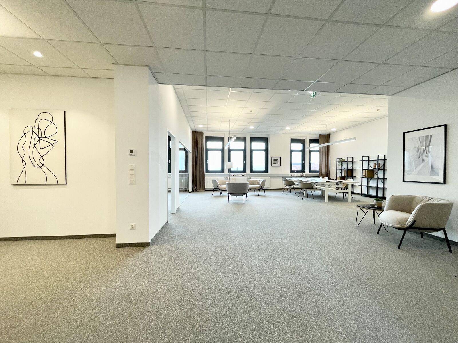 Geräumiger, offener Bürobereich mit Teppichboden, weißen Wänden und modernen Möbeln, ideal für flexible Arbeitsplätze.