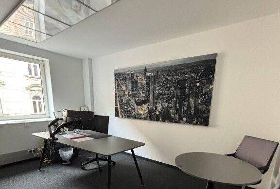 Einzelbüro mit einem Schreibtisch, zwei Monitoren und einem großen Stadtbild an der Wand als Dekoration.
