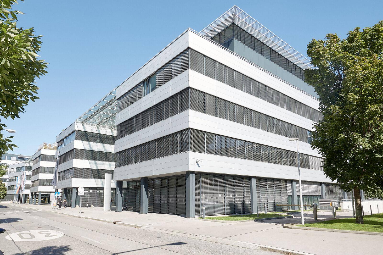 Eckansicht eines modernen Bürokomplexes mit großen Fenstern und Jalousien an einem sonnigen Tag.