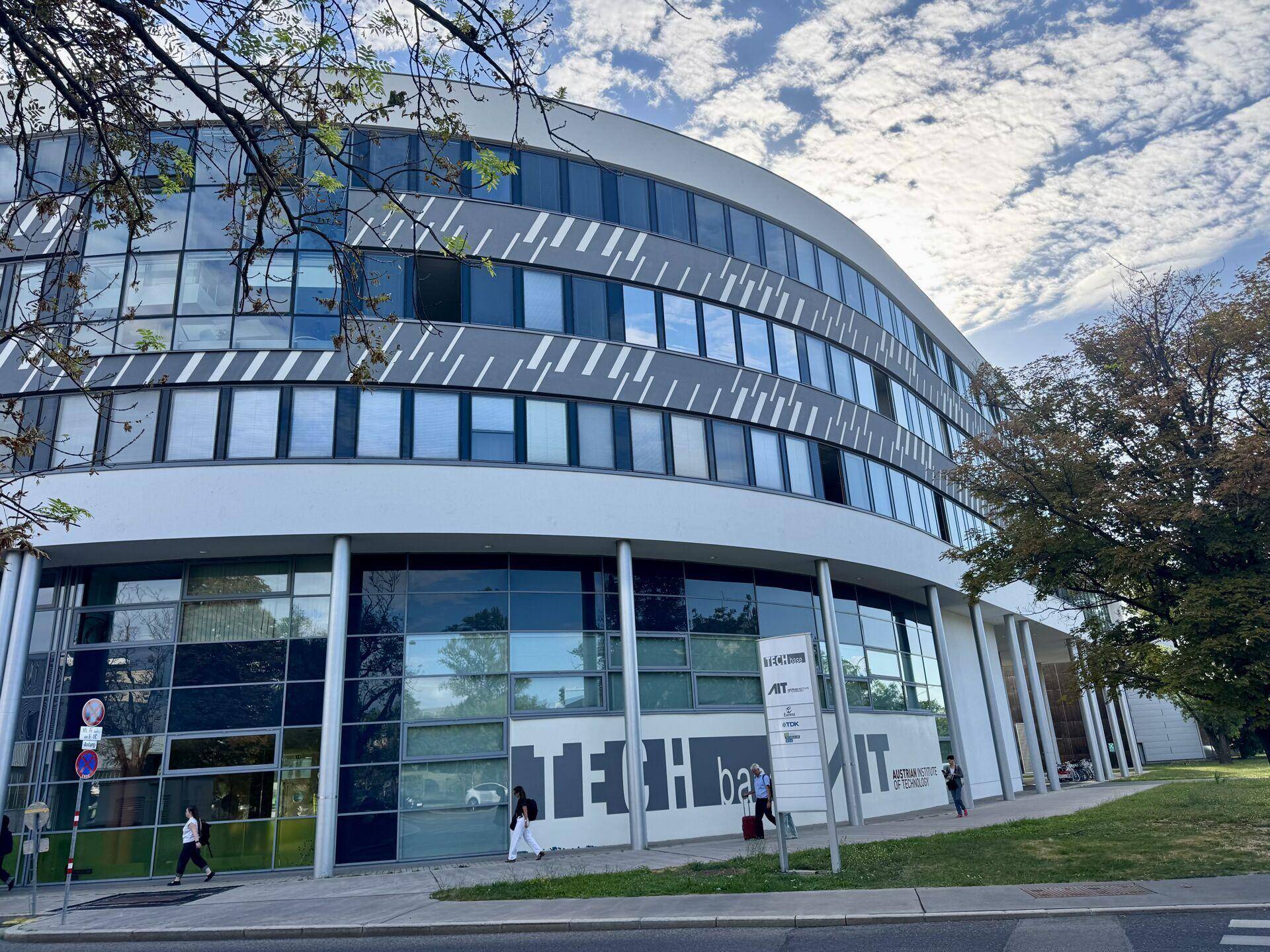 Nahaufnahme der modernen Bürogebäude-Fassade mit reflektierenden Fenstern und umliegender Grünfläche.