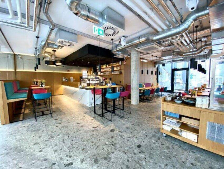 Moderner Café-Bereich mit industriellem Design, sichtbaren Lüftungsrohren und farbigen Hockern.