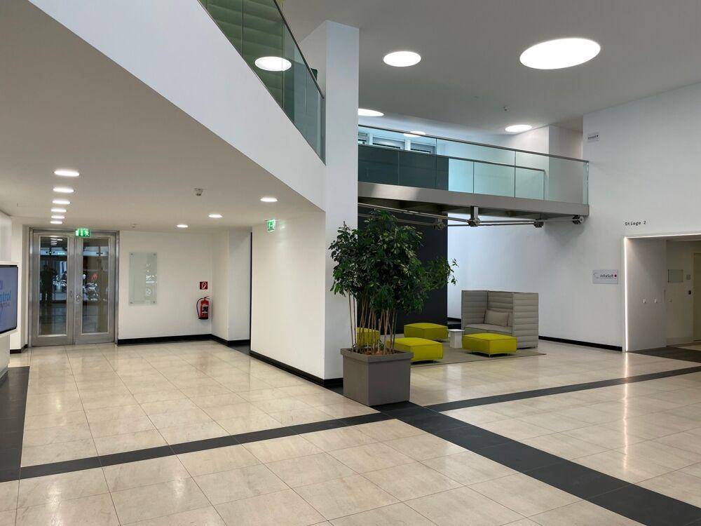 Heller, moderner Empfangsbereich mit Fliesenboden, Sitzgelegenheiten und offener Galerie.