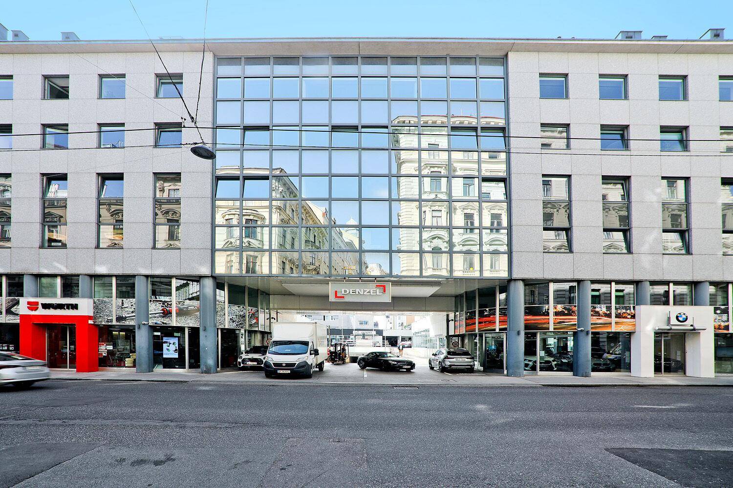 Moderne Geschäftsfassade mit großer Glasfront und Eingangsbereich, der den Blick auf weitere Gebäude freigibt.