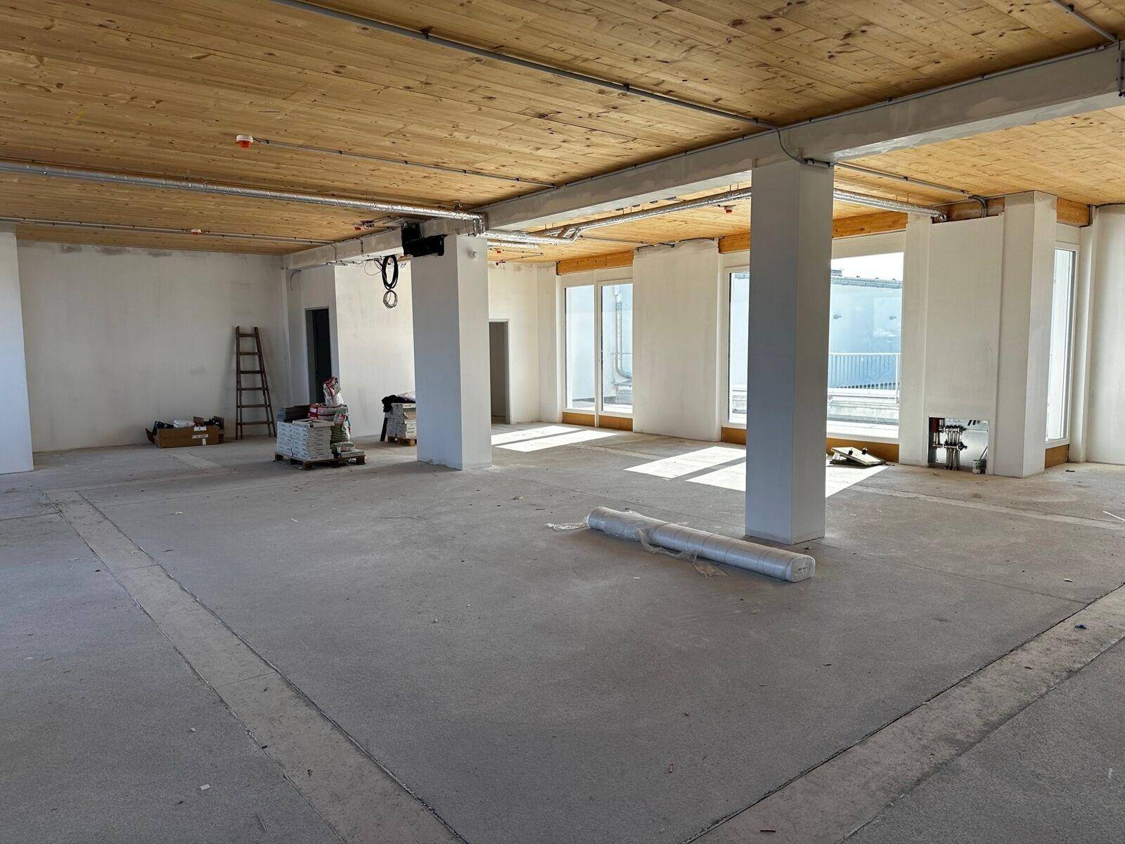 Weitläufiger Rohbau mit Holzbalkendecke und Betonboden, bereit für den Innenausbau mit viel Tageslicht.