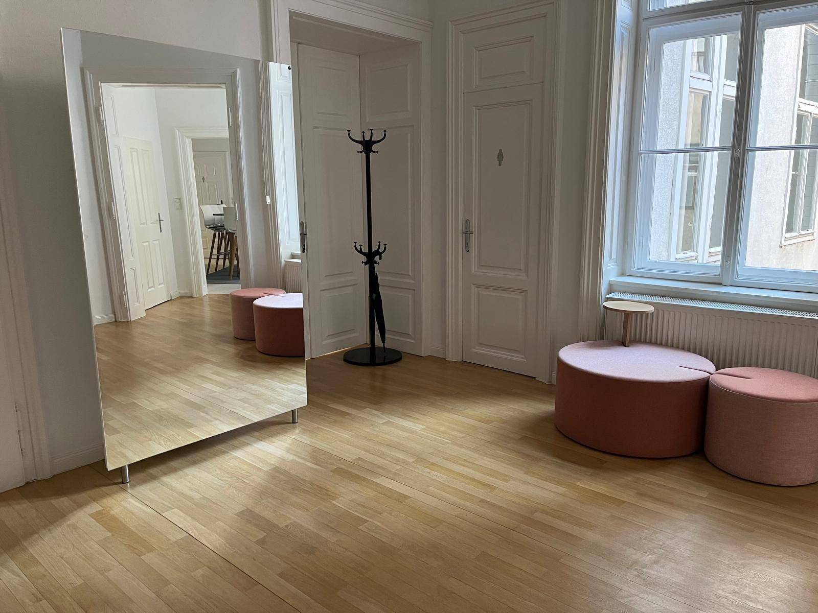 Heller Flur mit Holzboden, großem Spiegel und modernen Sitzgelegenheiten in Pastelltönen.