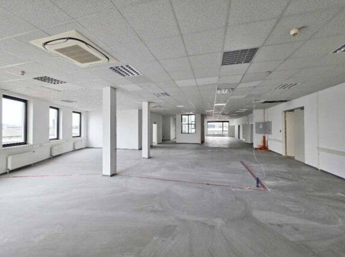 Großer, leerer Büroraum mit abgehängter Decke, Säulen und vielen Fenstern für Tageslicht.
