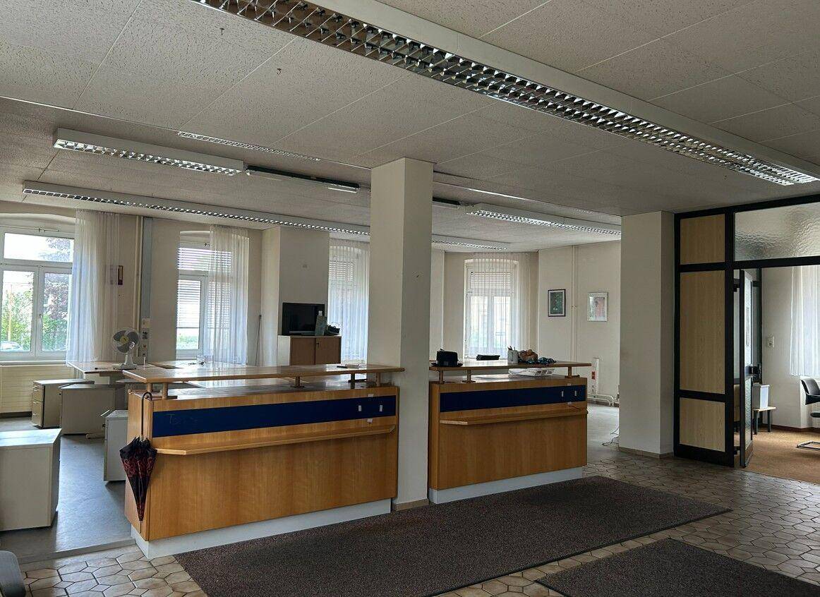 Großer Empfangsbereich in einem Bürogebäude mit gefliestem Boden und mehreren Schreibtischen.