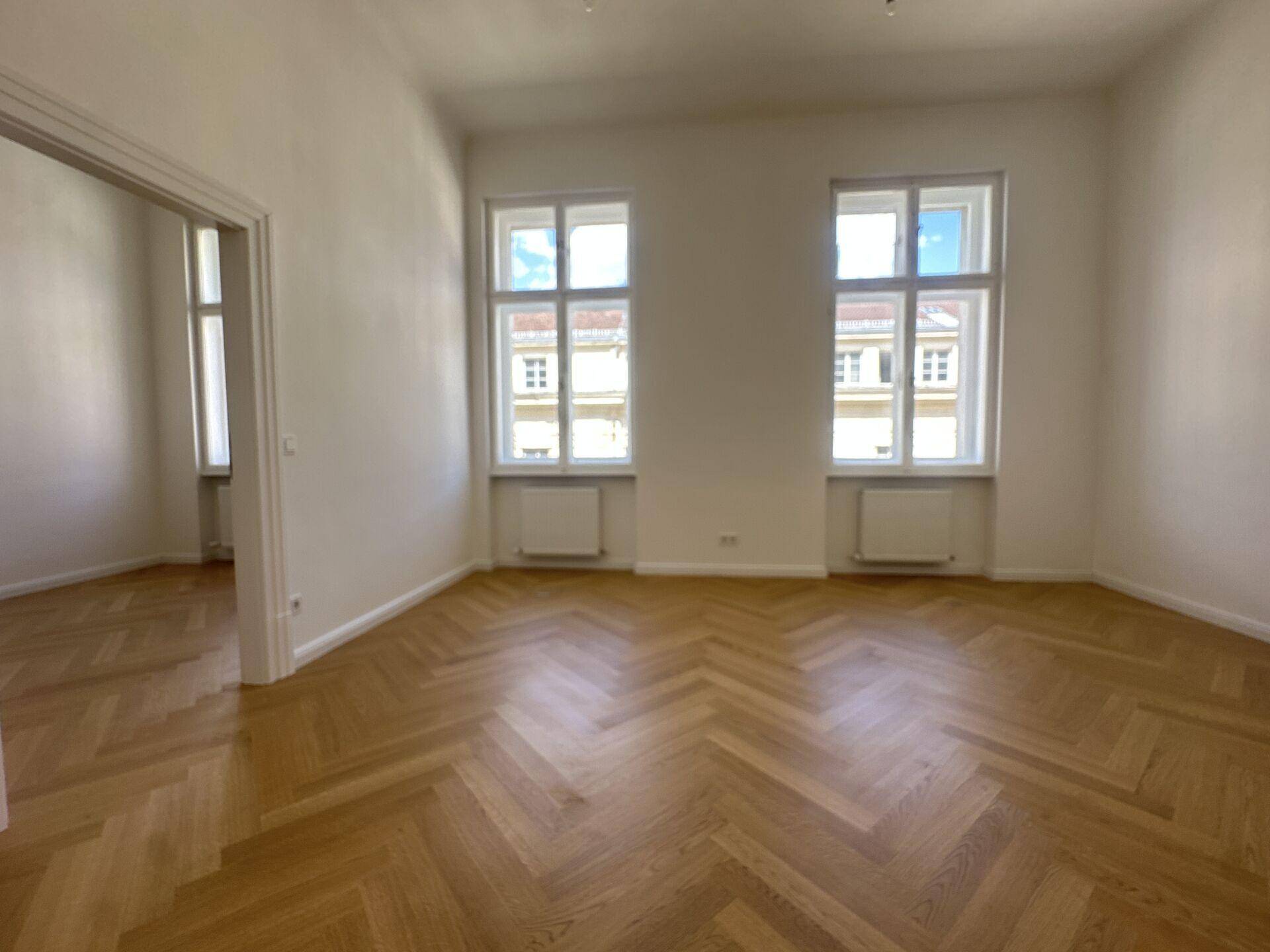 Heller Büroraum mit klassischem Fischgrätparkett und zwei großen Fenstern zur Straße.