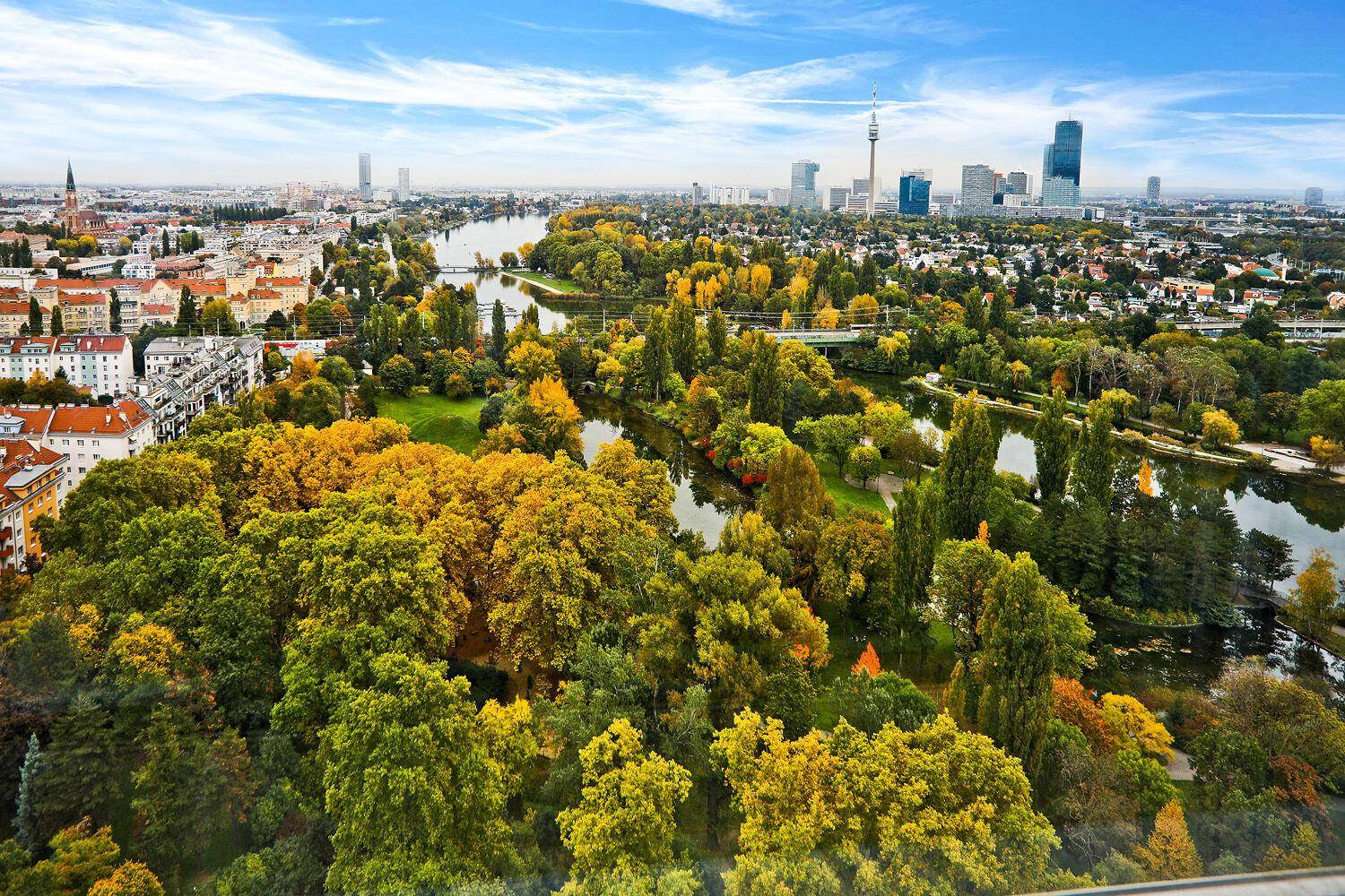 Weitläufige Stadtansicht mit Fluss, grünen Parks und moderner Skyline unter blauem Himmel.