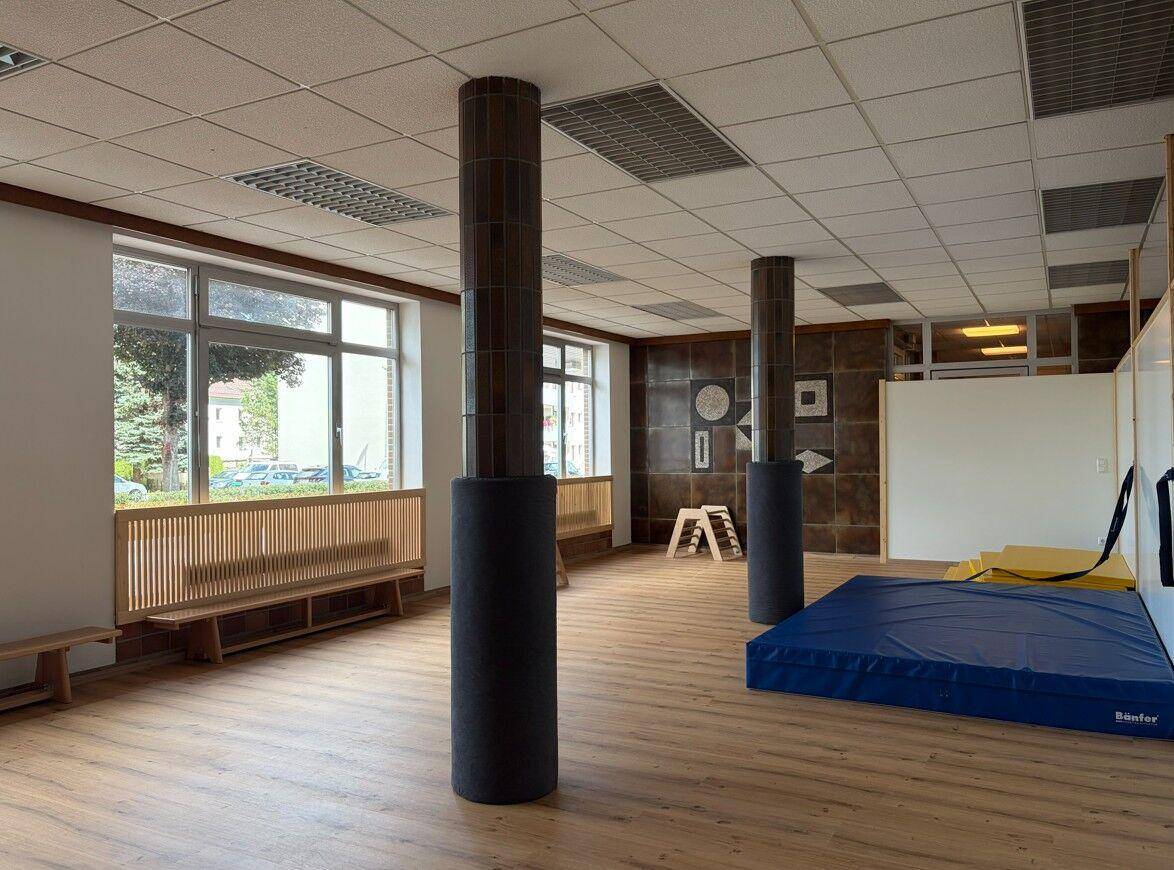 Großer Mehrzweckraum mit Holzboden, gepolsterten Säulen und Matten für sportliche Aktivitäten.