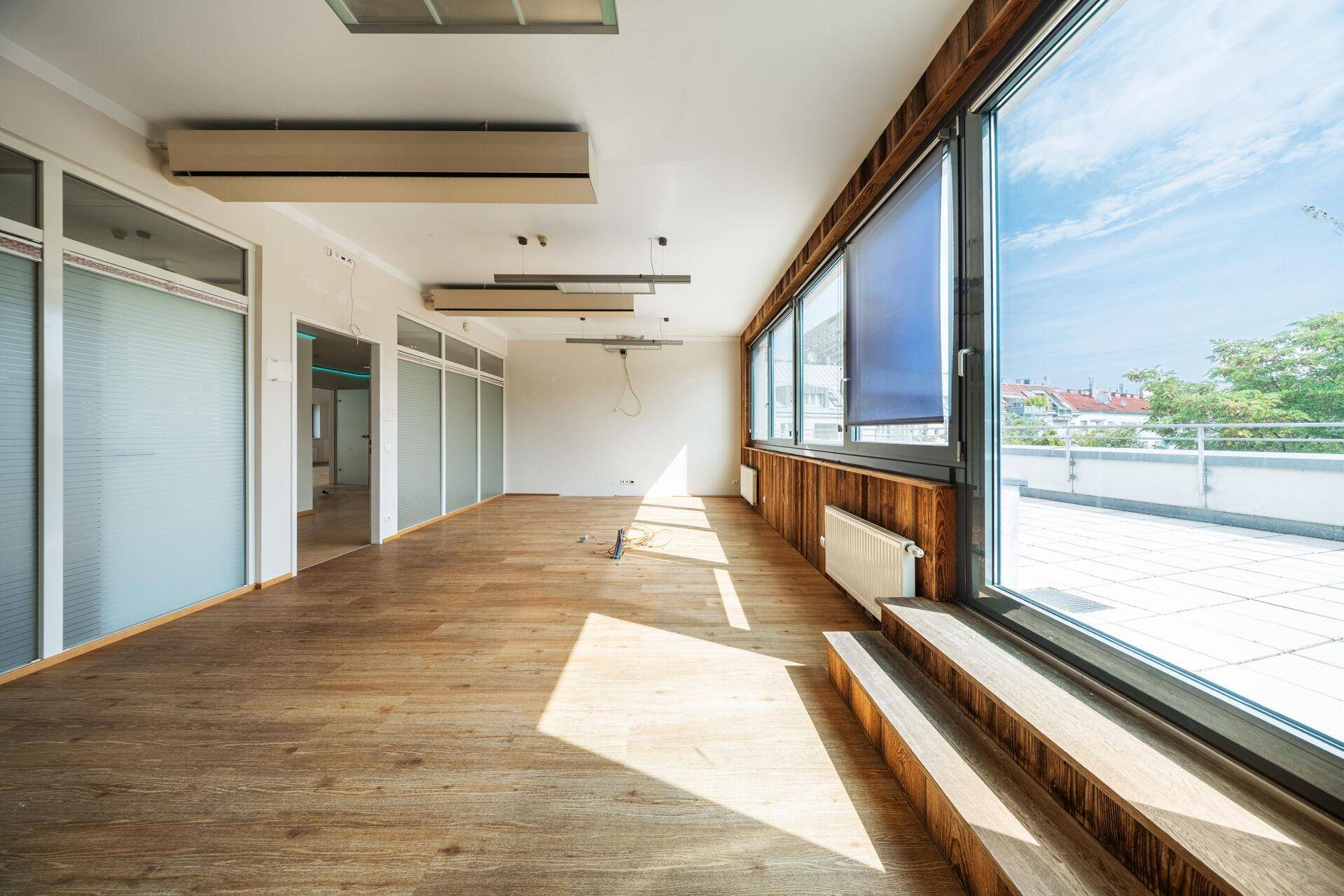 Geräumiger Büroraum mit Holzboden, großen Fenstern und Zugang zu einer Außenterrasse.
