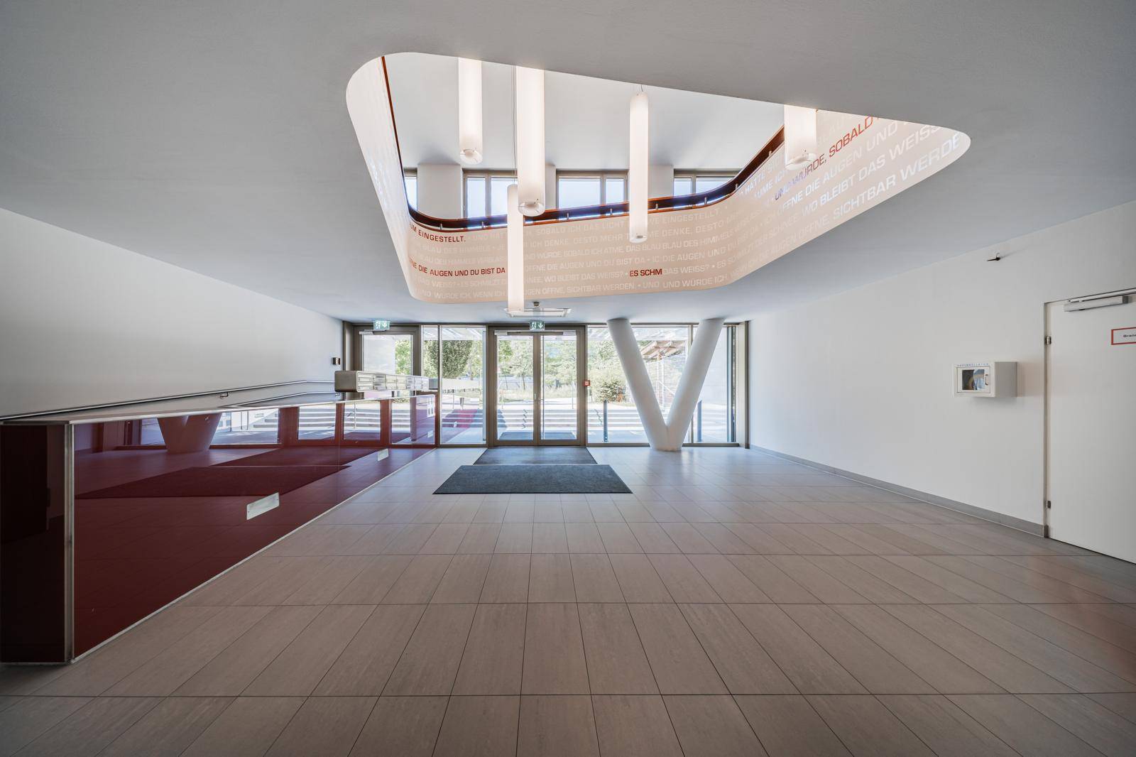 Moderne Eingangshalle mit hoher Decke, großen Glastüren und hellem Fliesenboden, einladend gestaltet und lichtdurchflutet.