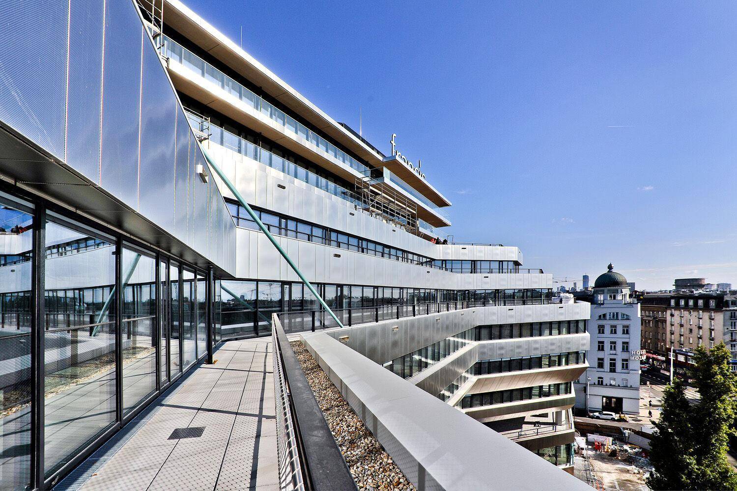 Moderne Gebäudefassade mit geschwungenen Linien und mehreren Terrassen, die einen weiten Blick bieten.