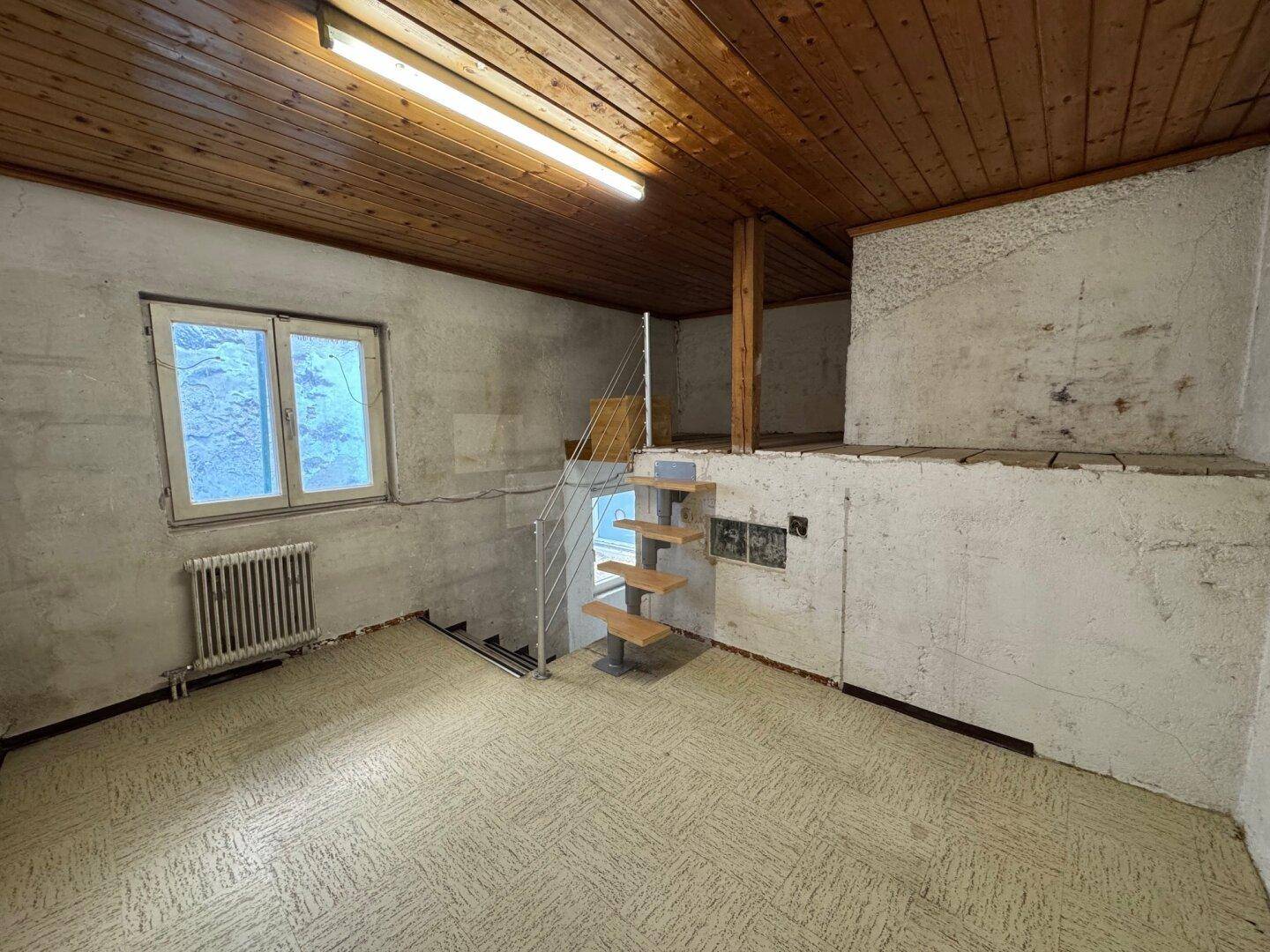 Rustikaler Kellerraum mit Holzbalkendecke, Betonwänden und einem kleinen Fenster.