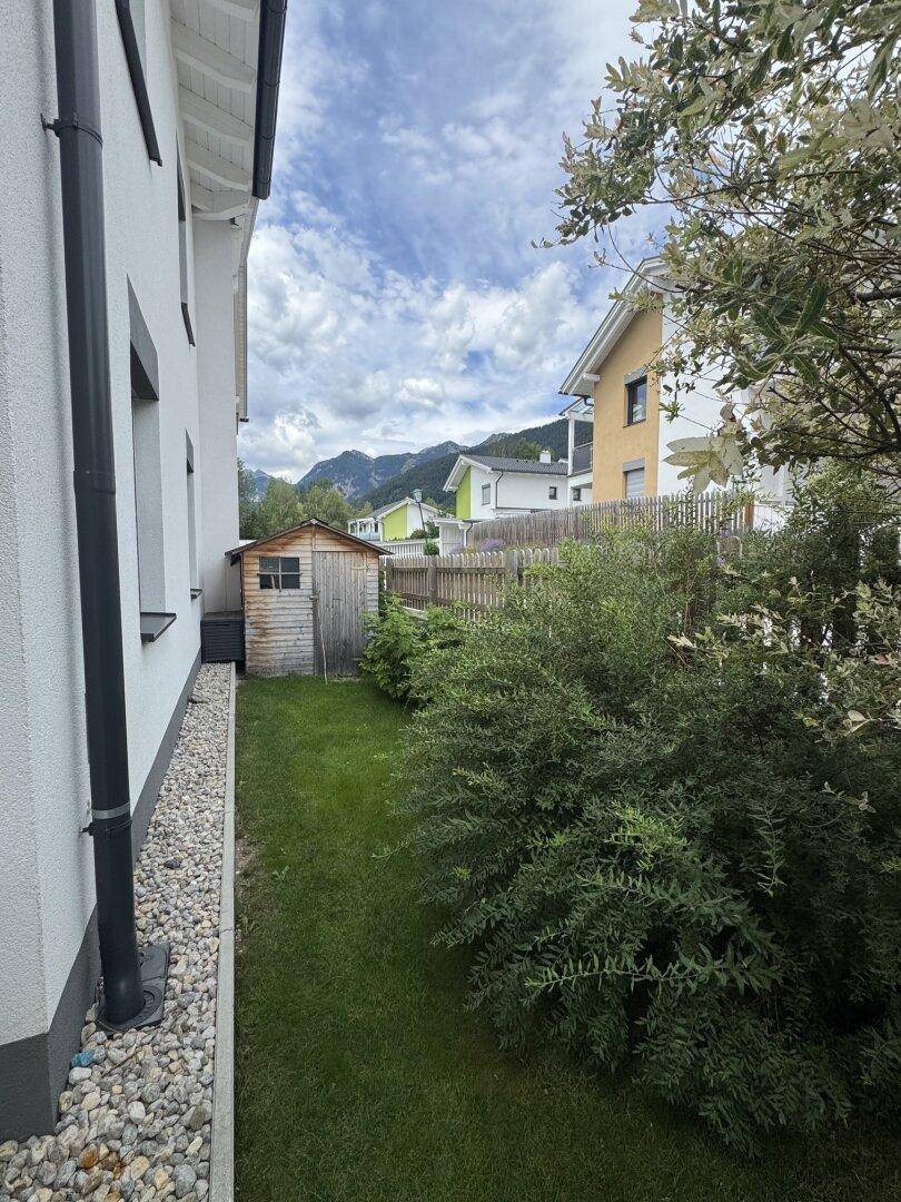 Seitlicher Gartenbereich mit Rasenfläche, Sträuchern und einem praktischen Gartenschuppen.