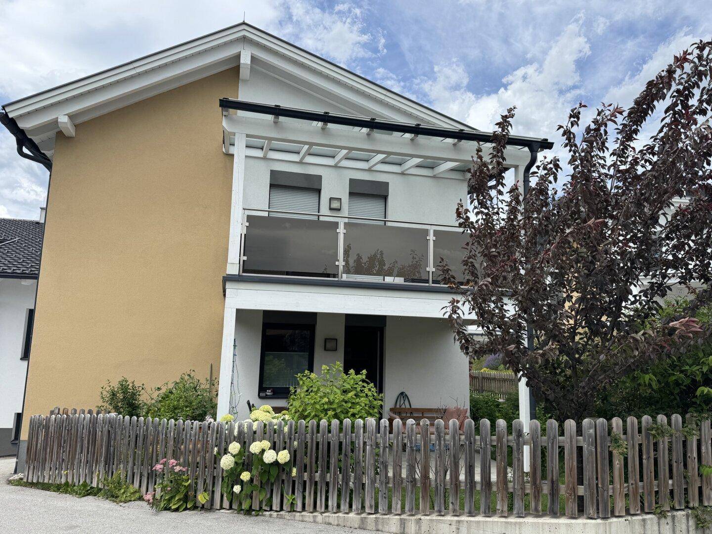 Ansicht des Hauses mit modernem Balkon im Obergeschoss und gelber Fassade.