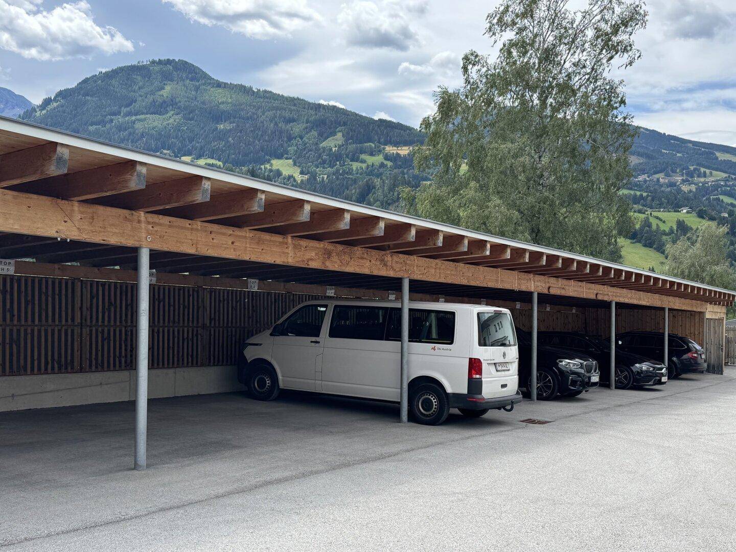 Überdachter Carport-Bereich mit mehreren Stellplätzen für Fahrzeuge, umgeben von Bergen.