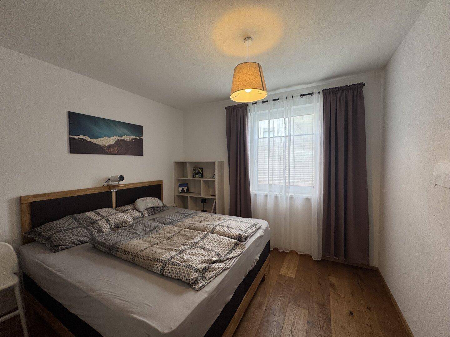 Gemütliches Schlafzimmer mit Holzboden, großem Doppelbett und Fenster mit Vorhängen.