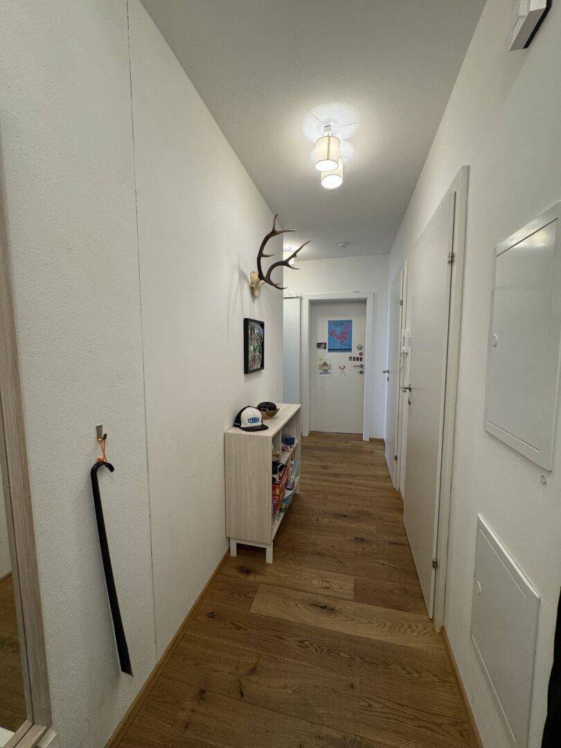 Heller Flur mit Holzboden, Garderobe und dekorativem Hirschgeweih an der Wand.