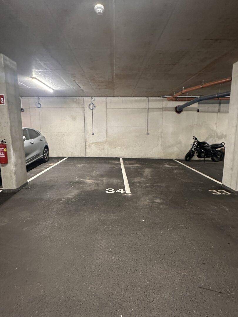 Innenansicht einer Tiefgarage mit nummerierten Stellplätzen und Betonwänden.