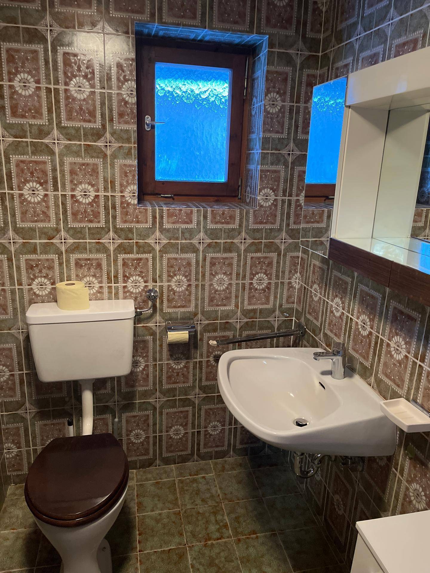 Badezimmer mit gemusterten Wandfliesen, Waschbecken, Toilette und Fenster für Tageslicht.