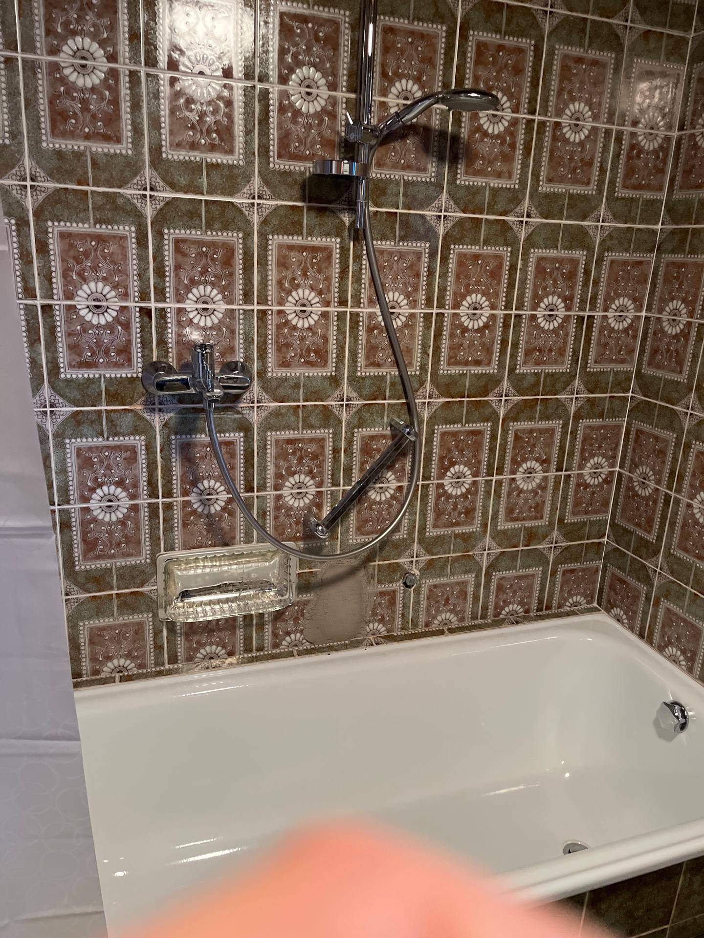 Badezimmer mit Badewanne und Duscharmatur, umgeben von traditionellen gemusterten Fliesen.