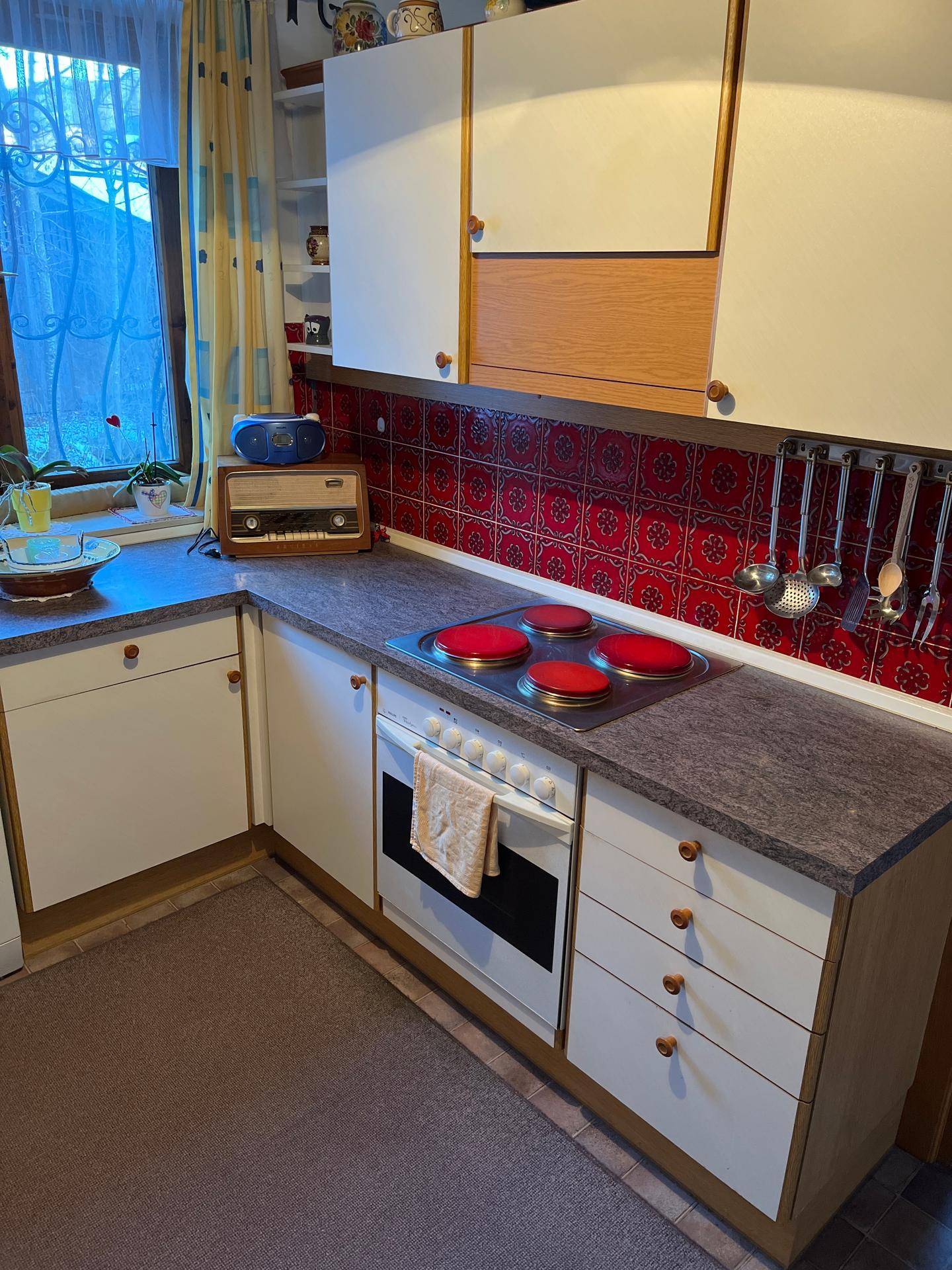 Traditionelle Küche mit weißen Schränken, rotem Fliesenspiegel und Elektroherd mit vier Kochplatten.