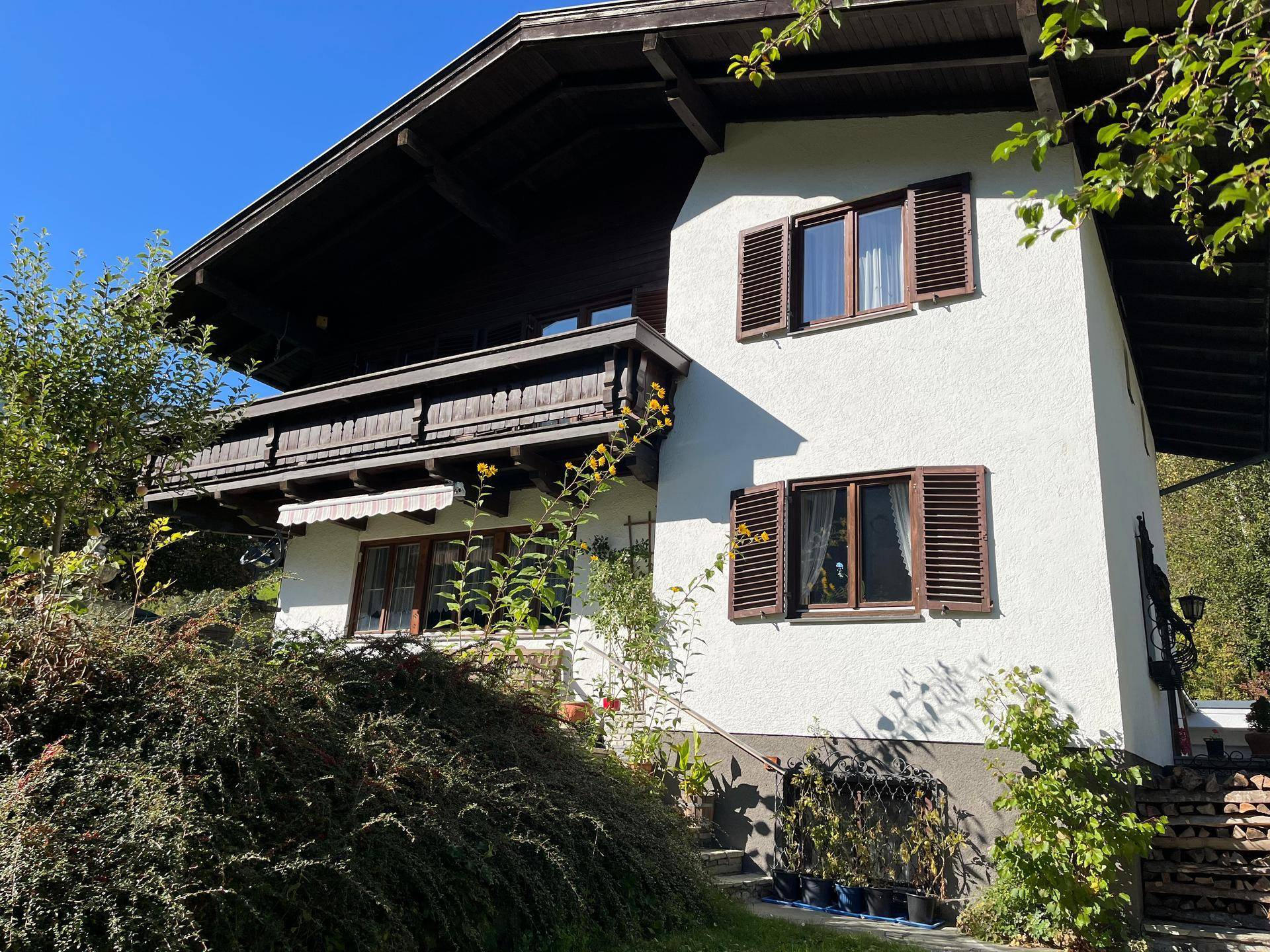 Traditionelles Haus mit Holzbalkon, Fensterläden und üppiger Vegetation in den Bergen.