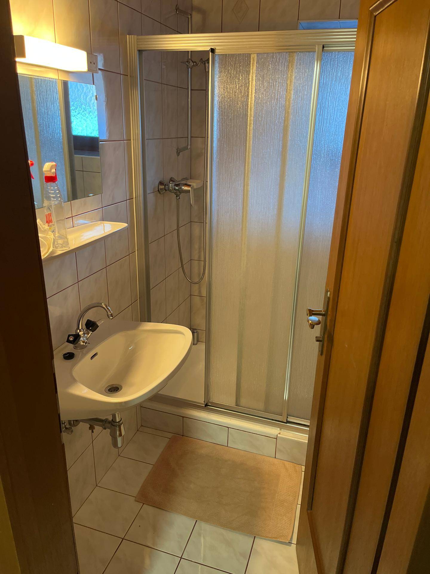 Kleines Badezimmer mit Duschkabine, Waschbecken und hellen Fliesen, funktional eingerichtet.