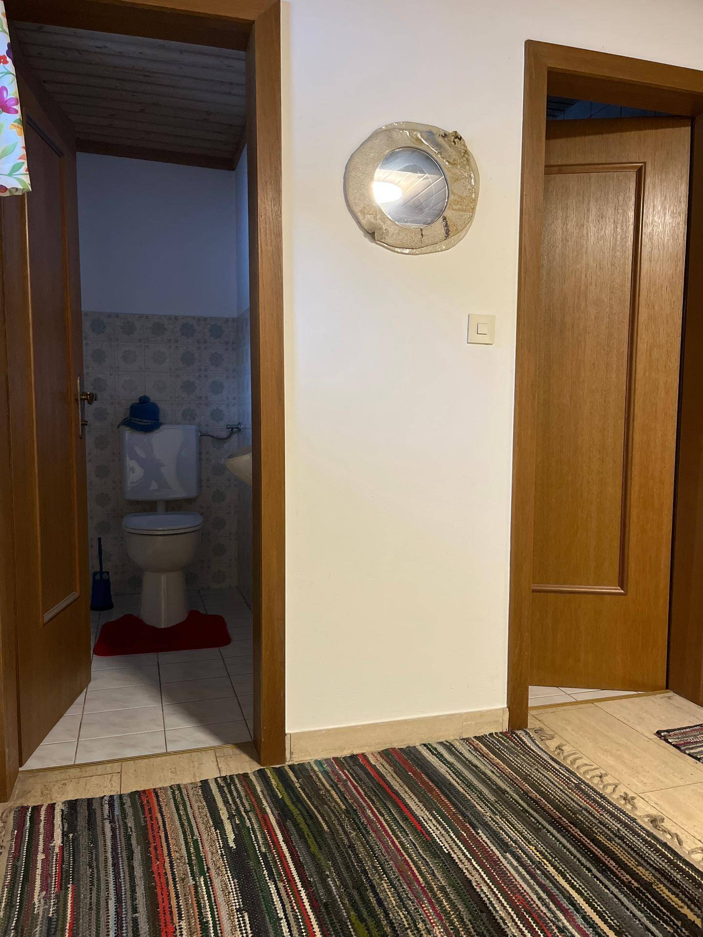 Flur mit Zugang zu einem WC, gekennzeichnet durch eine Holztür und gemusterte Fliesen.