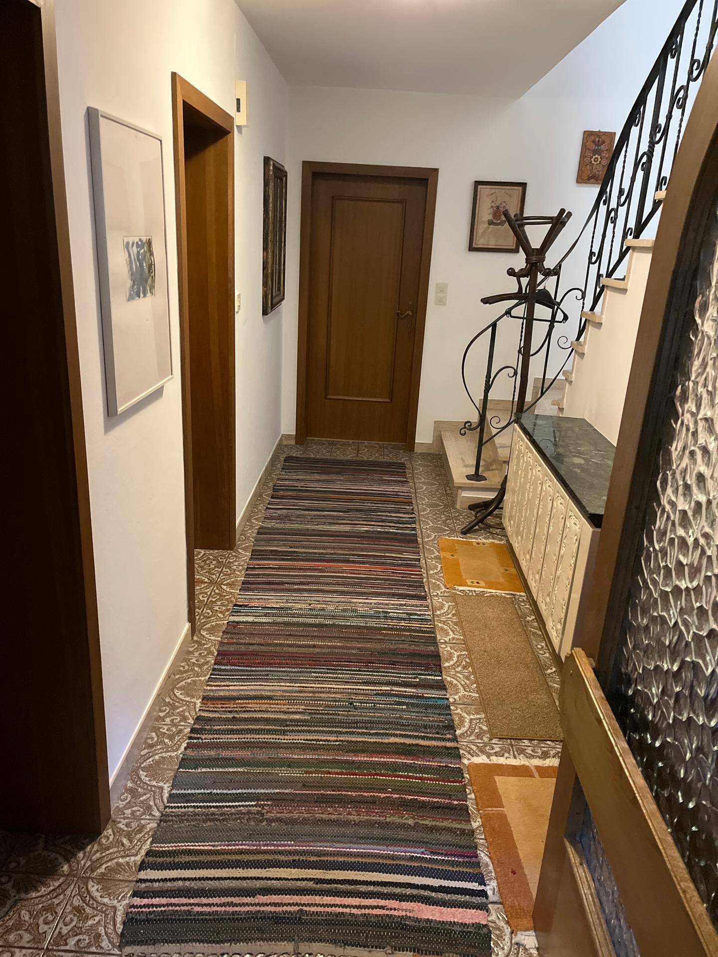 Heller Flur mit gemusterten Fliesen, Holzvertäfelung und schmiedeeisernem Treppengeländer.