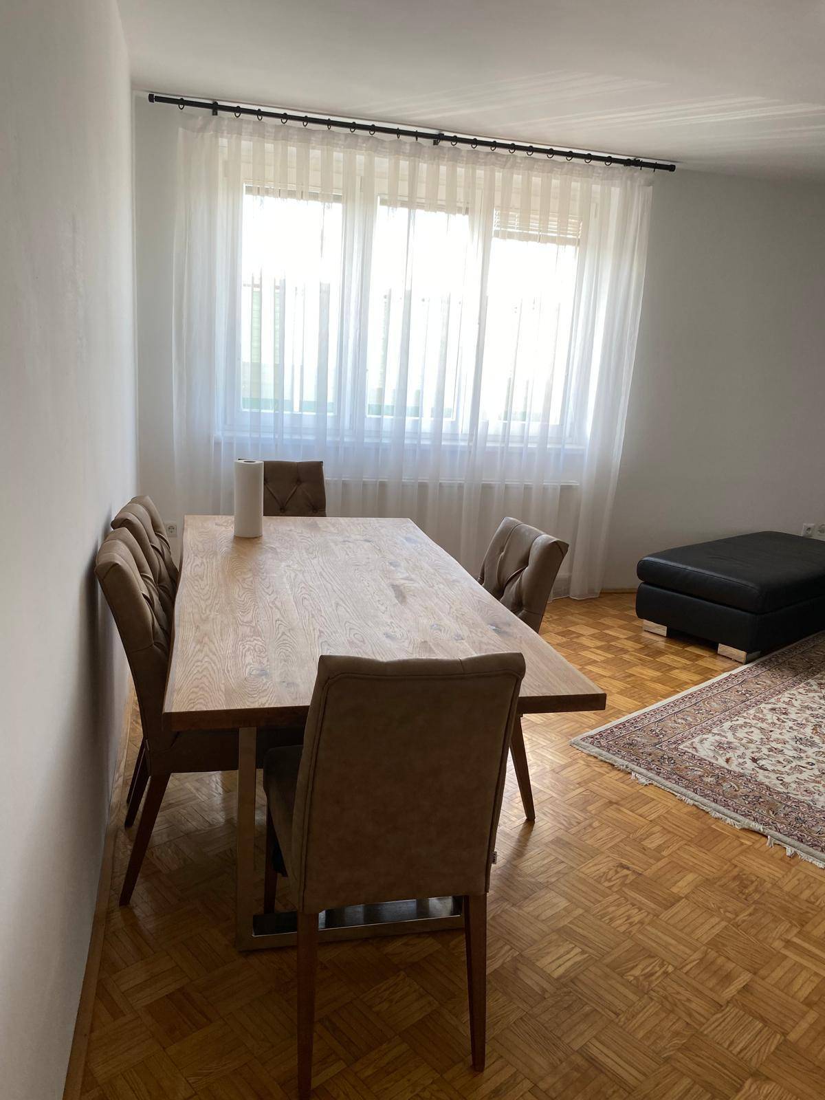 Essbereich mit großem Holztisch und bequemen Stühlen neben einem Fenster mit Vorhängen.