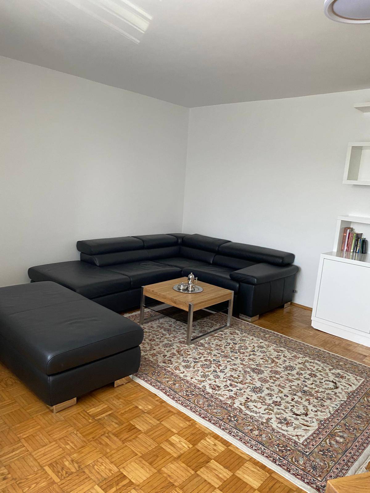 Gemütliches Wohnzimmer mit schwarzem Ecksofa, Couchtisch und Teppich auf Parkettboden.