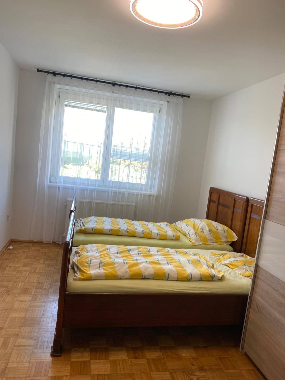 Schlafzimmer mit zwei Einzelbetten, Parkettboden und einem Fenster mit viel Tageslicht.
