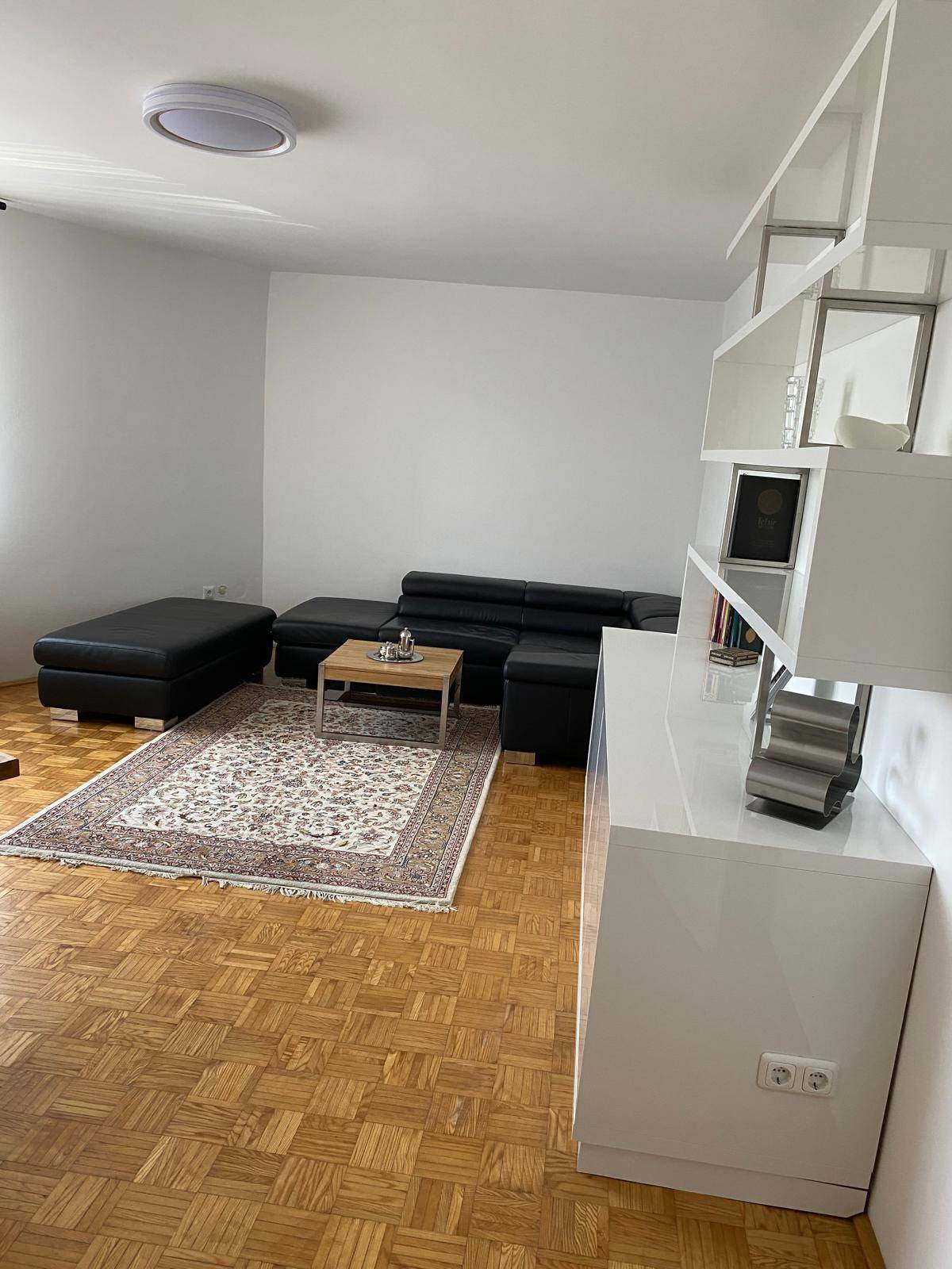Helles Wohnzimmer mit schwarzem Sofa, Teppich und modernem weißen Regalsystem.